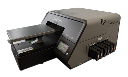 Versatile, fast, reliable – the RICOH Ri 1000X for growing demands RICOH Ri 1000X with open print platen, touchscreen control panel, and side-mounted ink system – versatile DTG printer for personalized textiles in medium runs