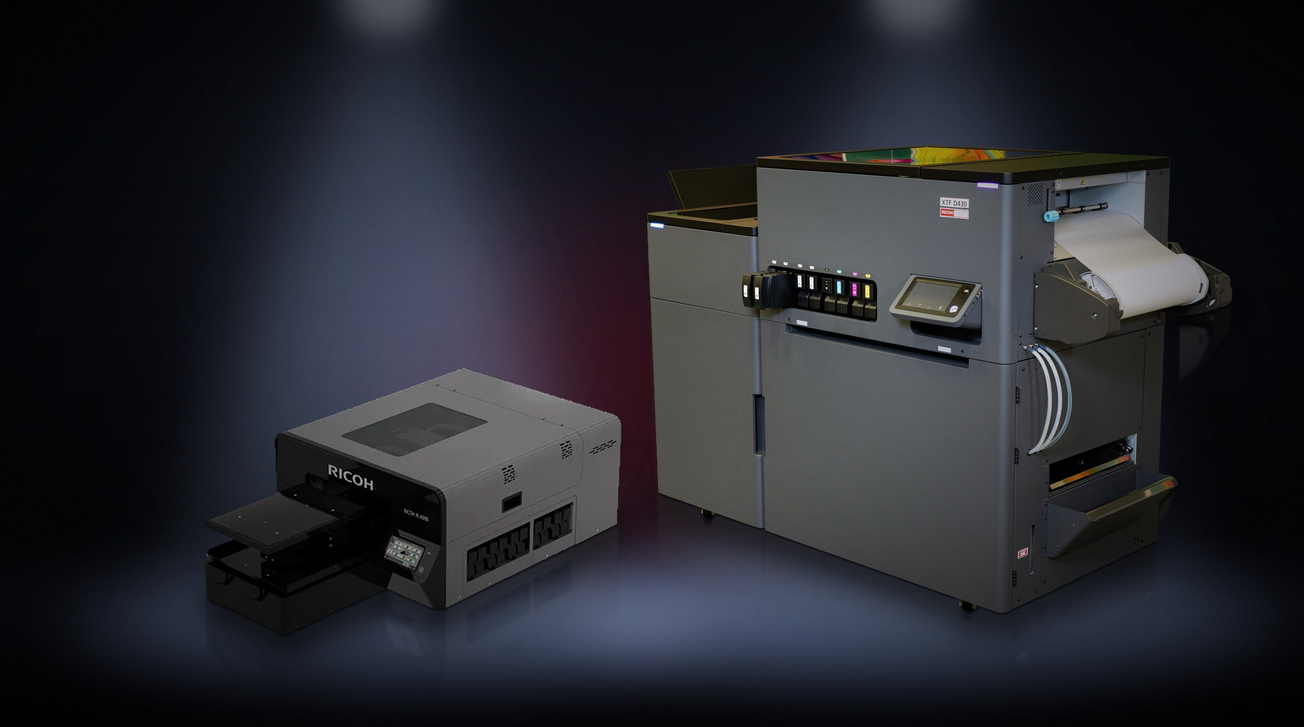 Two Ricoh printing systems, a small DTG printer and a larger transfer printing system with display and paper roll.